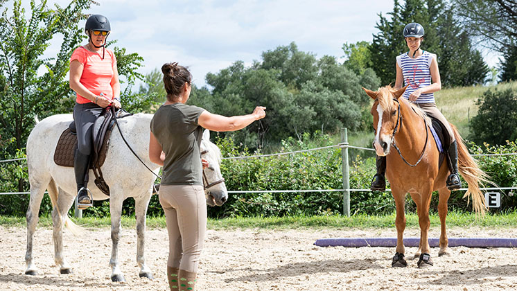 three riders on horseback wearing helmets and an instructor on the ground